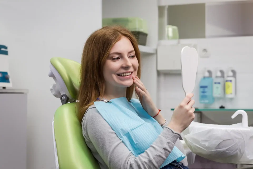 Woman sitting in a dental chair examining dentures with a handheld mirror in Fenton, MO